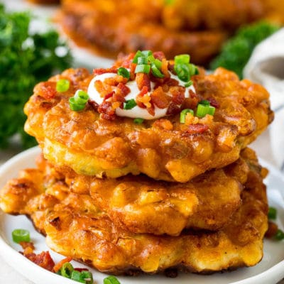 A stack of corn fritters topped with bacon, sour cream and green onions.