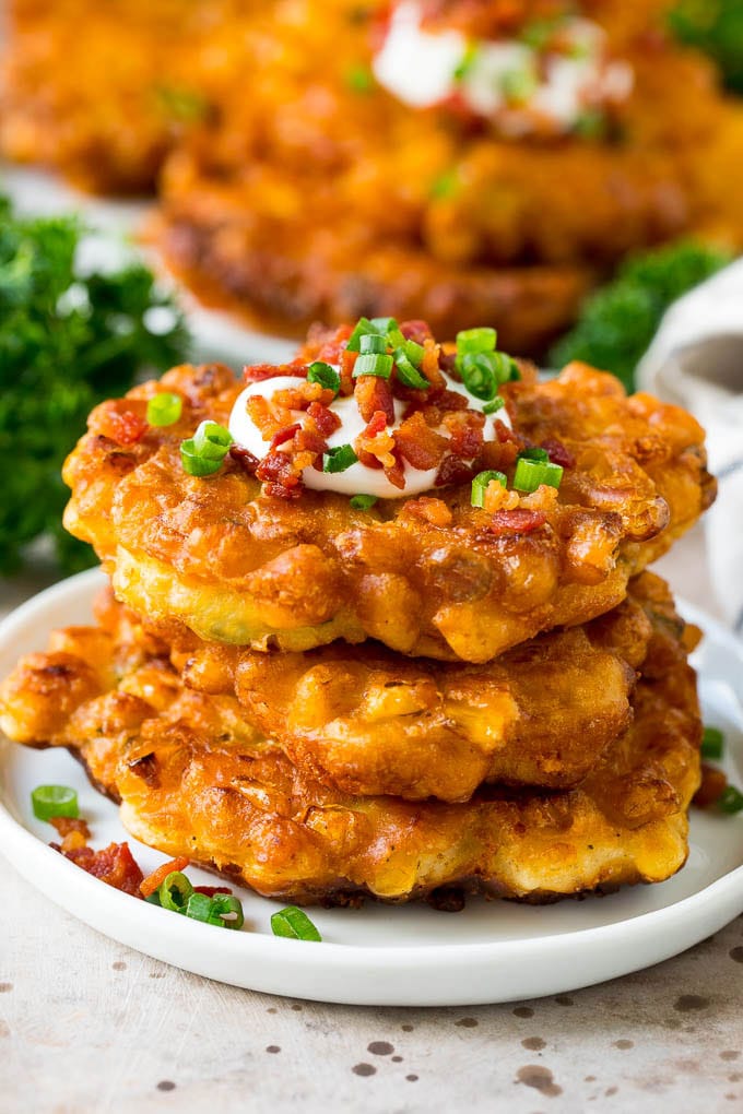 A stack of corn fritters topped with bacon, sour cream and green onions.