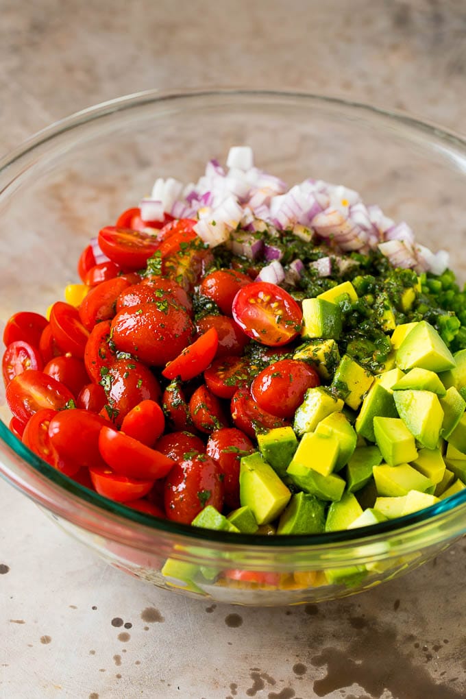 Dressing poured over tomatoes, corn and avocado in a salad bowl.