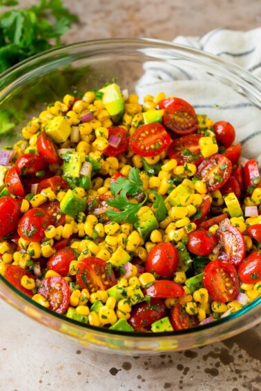 A bowl of corn salad with avocado and tomato, all tossed in a lime dressing.