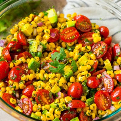 A bowl of corn salad with avocado and tomato, all tossed in a lime dressing.