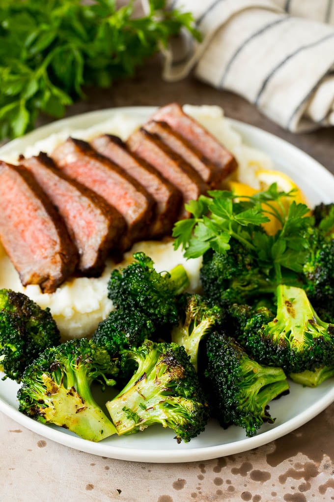 Grilled broccoli on a plate with steak and mashed potatoes.