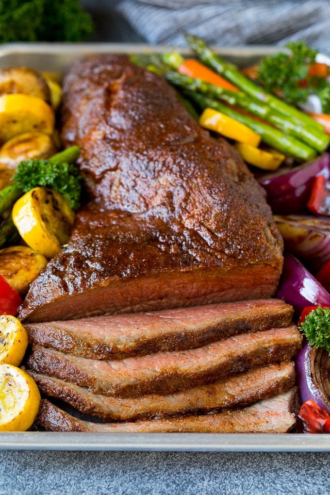 Smoked tri tip sliced and served on a pan with grilled vegetables.