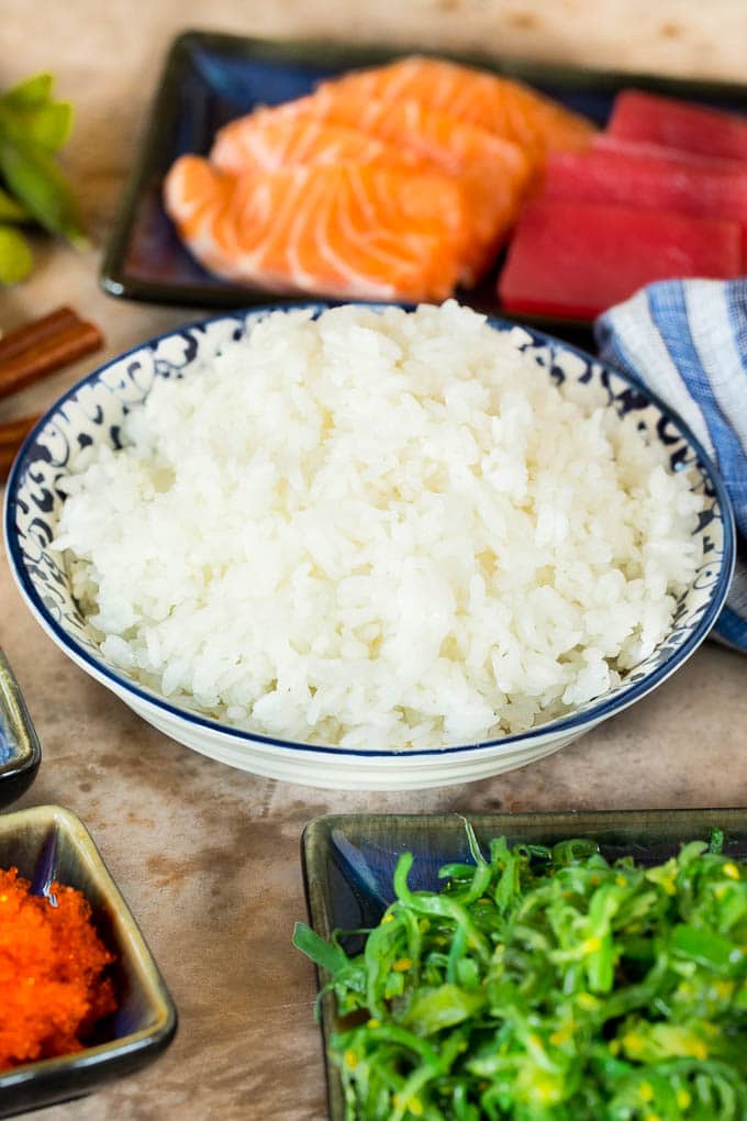 A bowl of sushi rice served with sashimi and seaweed salad.