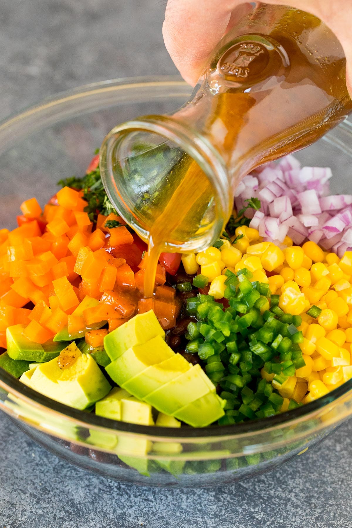 Dressing being poured over a vegetable and bean salad.