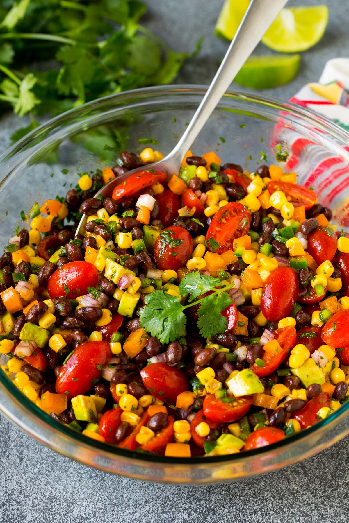 A bowl of black bean salad with a serving spoon in it.