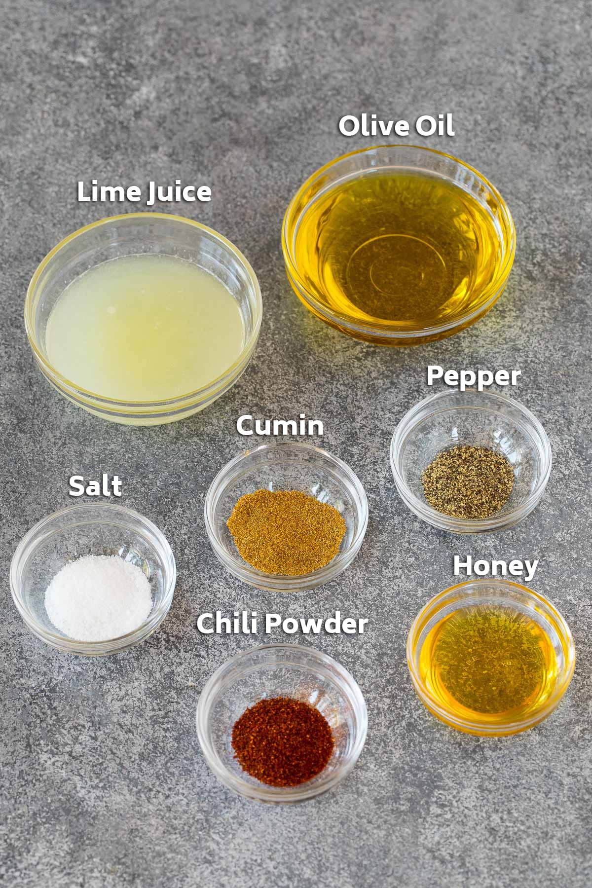 Bowls of salad dressing ingredients including olive oil, lime juice and spices.