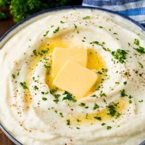 A bowl of cauliflower mashed potatoes topped with melted butter and parsley.