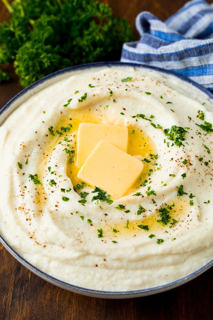 A bowl of cauliflower mashed potatoes topped with melted butter and parsley.