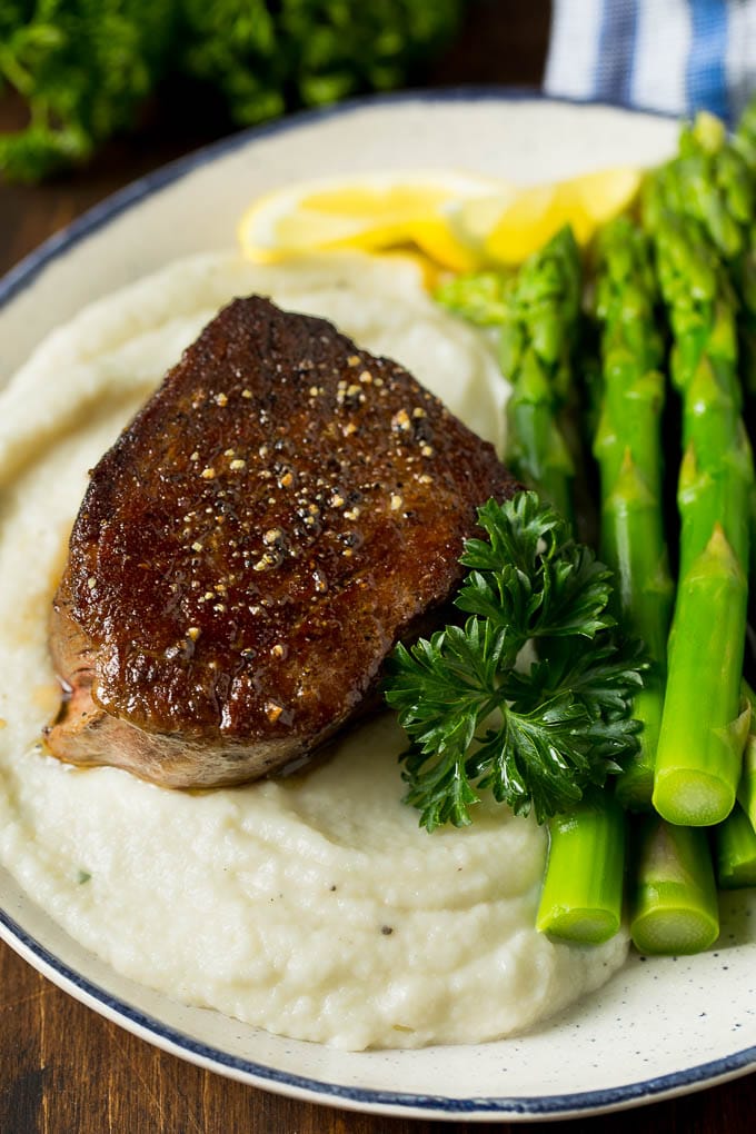 Cauliflower mashed potatoes on a plate with steak and asparagus.