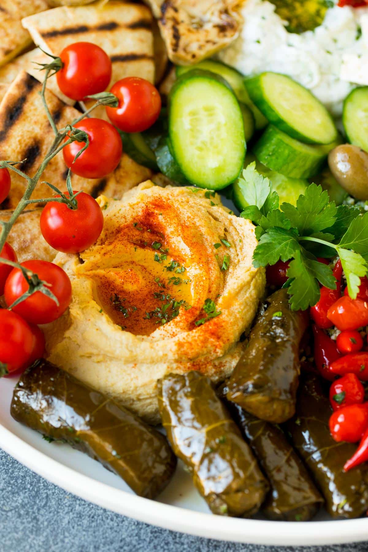 Homemade hummus on a plate with tomatoes, stuffed grape leaves and cucumbers.