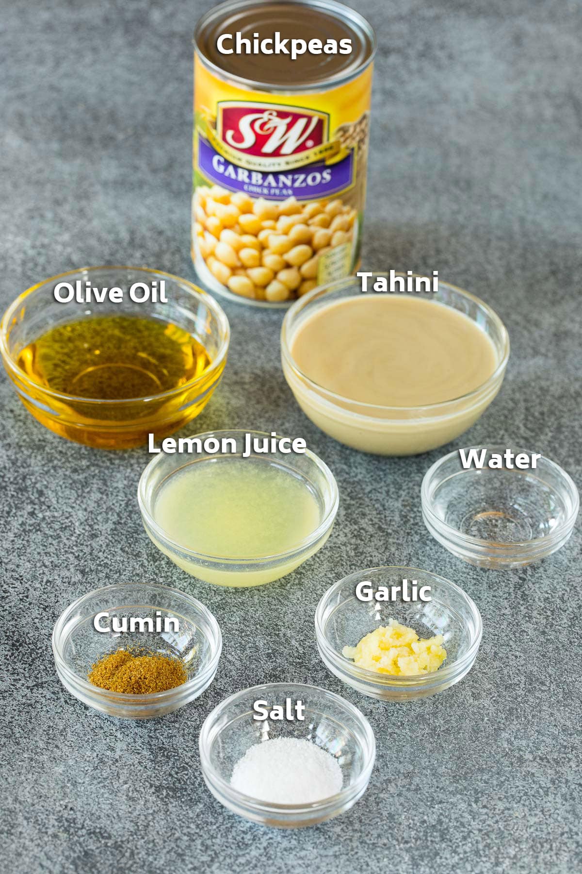 Ingredients including a can of chickpeas, and bowls filled with lemon juice, tahini, olive oil and spices.