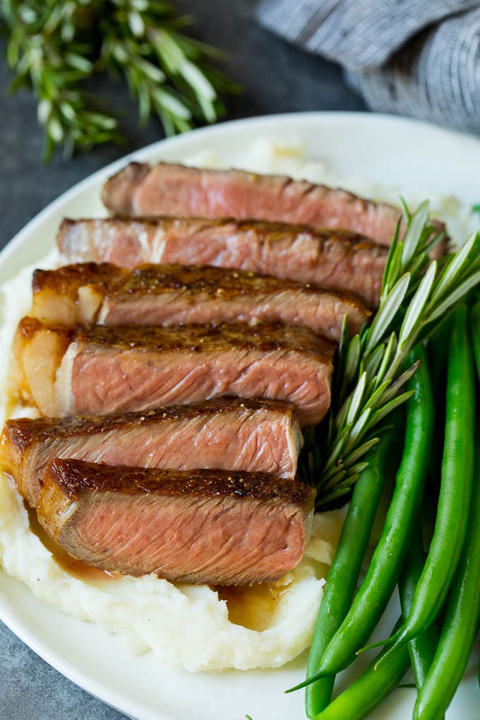 Sliced rib eye steak served with mashed potatoes and green beans.