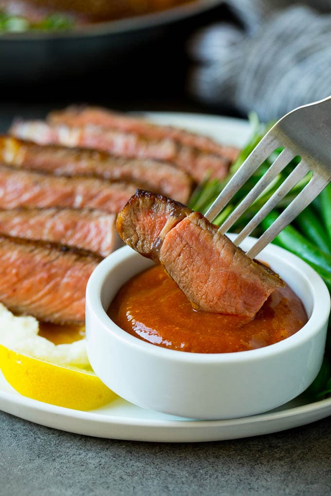 A fork dipping a piece of meat into steak sauce.