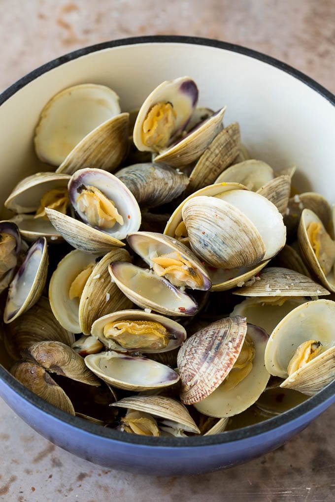This steamed clams recipe is fresh shellfish cooked with garlic, butter, herbs and lemon. Cooked clams in a blue pot.
