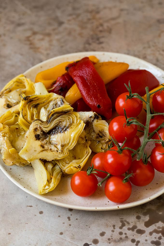 Roasted peppers, grilled artichokes and cherry tomatoes on a plate.