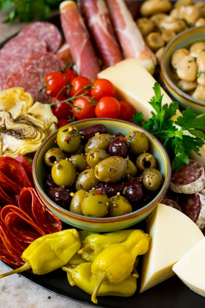 A close up of an antipasto platter with a bowl of olives, pickled vegetables, meats and cheeses.