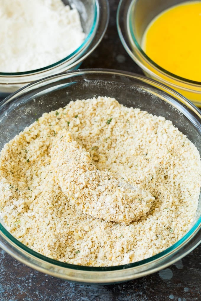 A piece of chicken in a bowl of parmesan breadcrumbs.