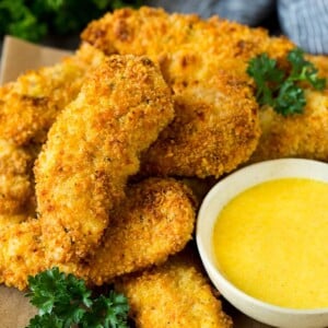 A plate of baked chicken tenders with a side of honey mustard.