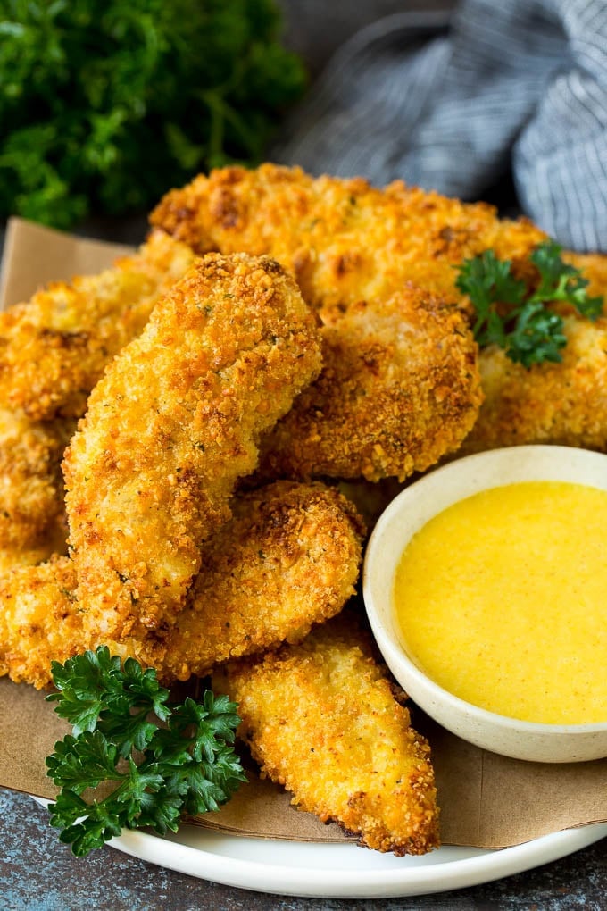 A plate of baked chicken tenders with a side of honey mustard.