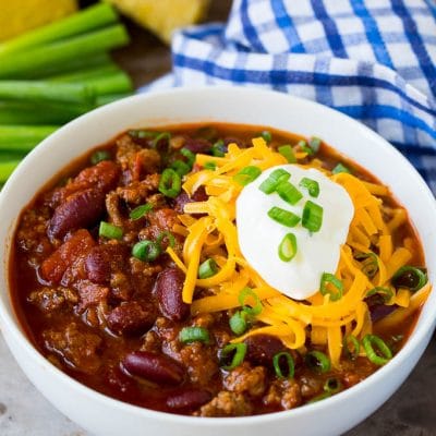 A bowl of beef chili topped with cheese, sour cream and green onions.