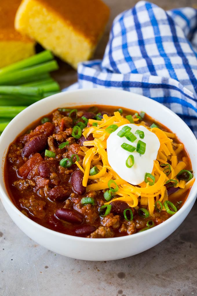 A bowl of beef chili topped with cheese, sour cream and green onions.