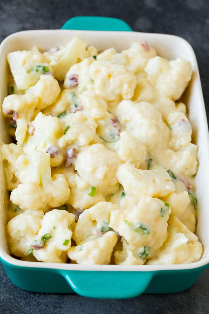 Florets tossed with cheese sauce, bacon and green onions in a dish.