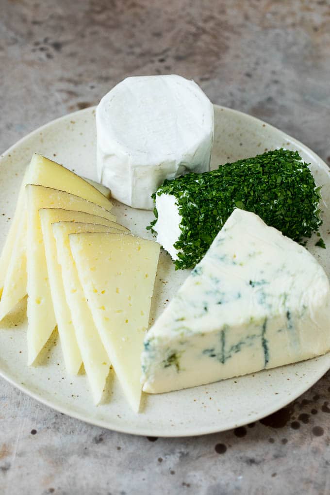 A complete guide on how to put together the best charcuterie board, with a selection of meats, cheeses, crackers, fruit, veggies and other snack foods. Four different types of cheese arranged on a plate.