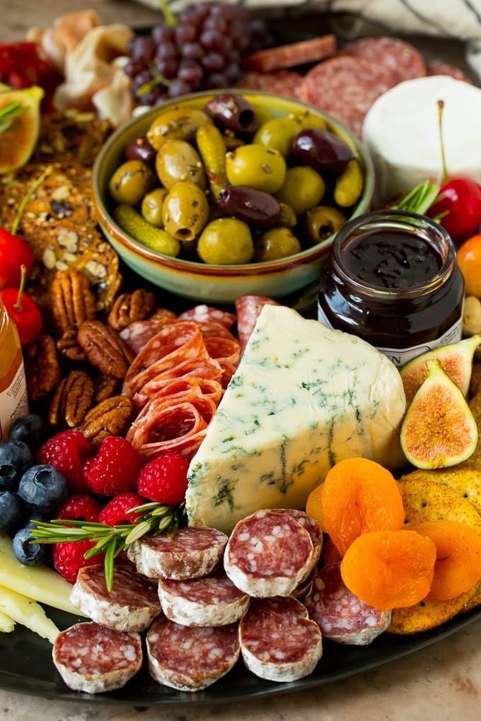 A charcuterie board close up with a wedge of cheese surrounded by salami, fruit and nuts.