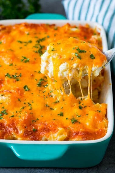 A spoon serving up a portion of cheesy potatoes topped with chopped parsley.