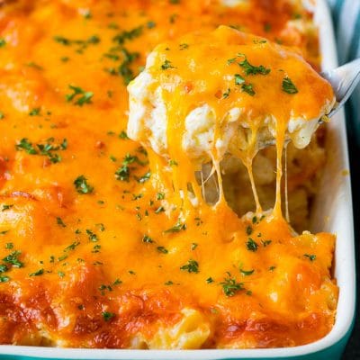 A spoon serving up a portion of cheesy potatoes topped with chopped parsley.