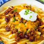A skillet of chili cheese fries topped with sour cream and green onions.