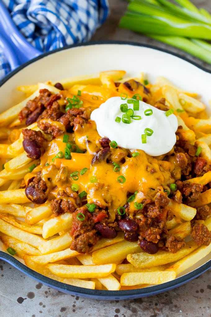 A skillet of chili cheese fries topped with sour cream and green onions.