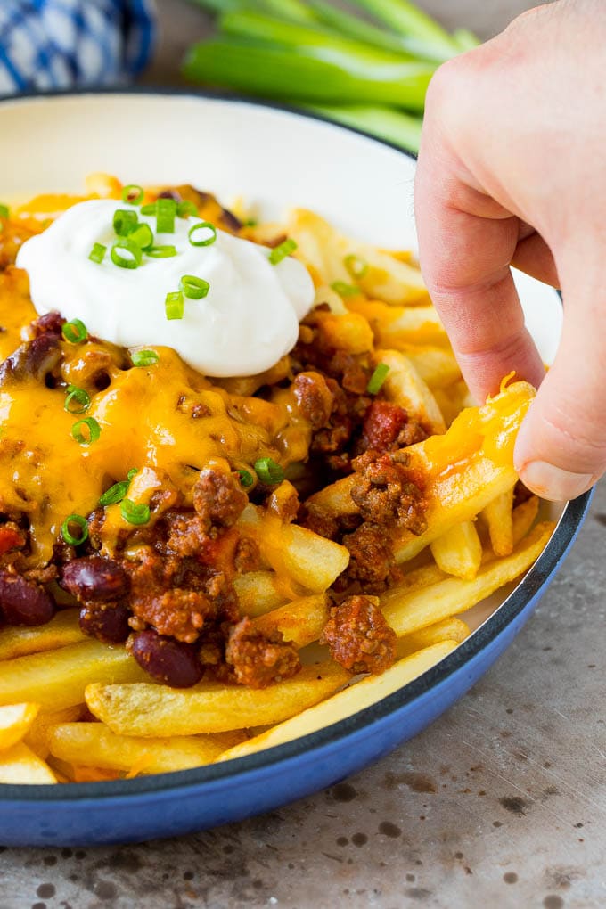 A hand reaching for chili cheese fries.