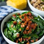 A bowl of collard greens next to a bowl of black eyed peas and cornbread.