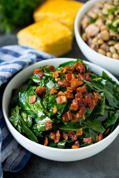 A bowl of collard greens next to a bowl of black eyed peas and cornbread.