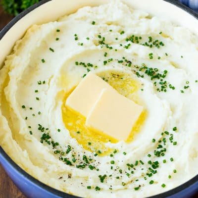 A pot of cream cheese mashed potatoes topped with butter and chives.