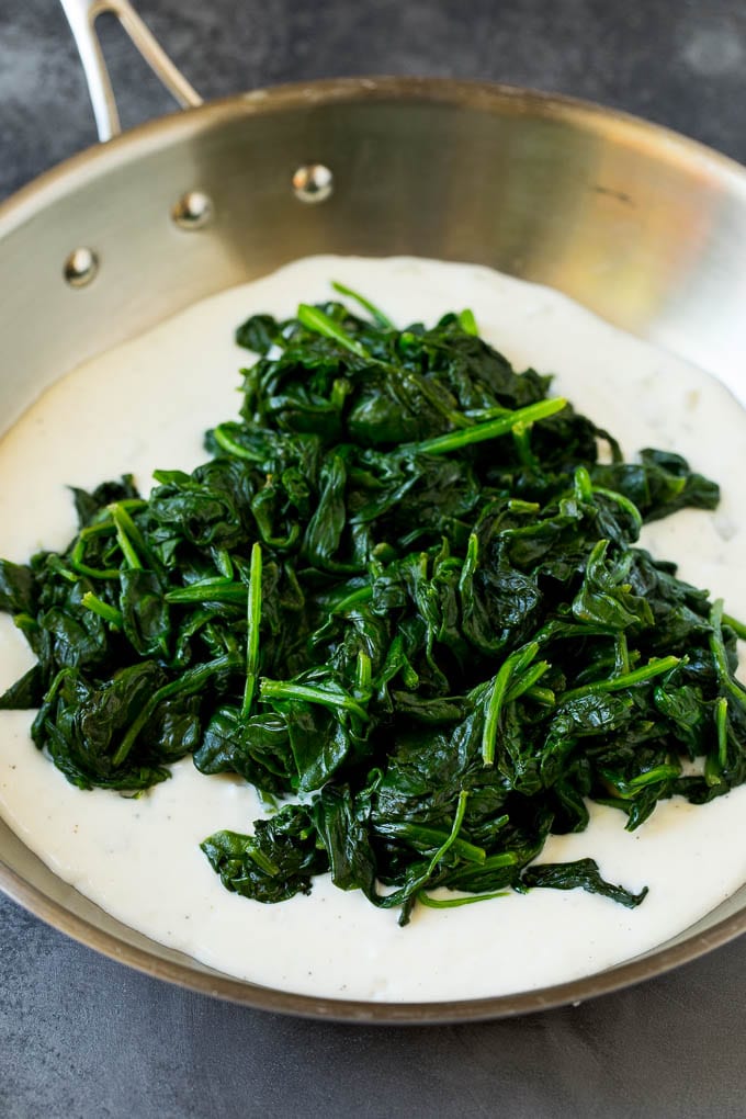 This creamed spinach is fresh sauteed spinach leaves in a flavorful cream sauce with parmesan cheese. Cream sauce in a pan with a pile of cooked greens on top.