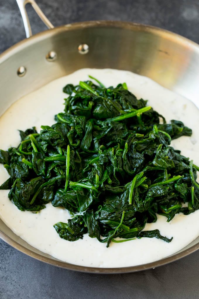 Cream sauce in a pan with a pile of cooked greens on top.