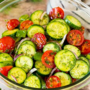 A bowl of cucumber tomato salad garnished with fresh herbs.