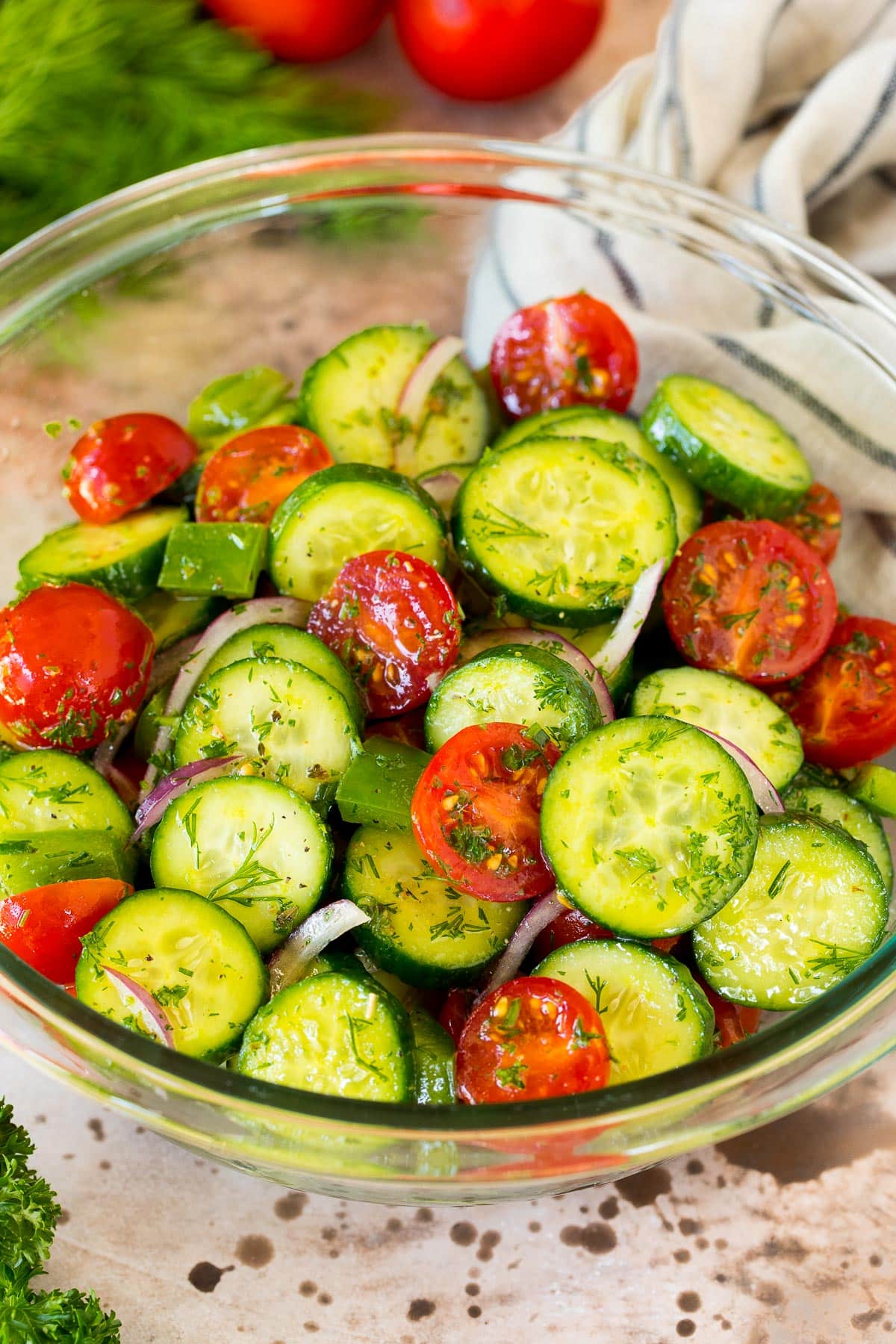A bowl of cucumber tomato salad garnished with fresh herbs.