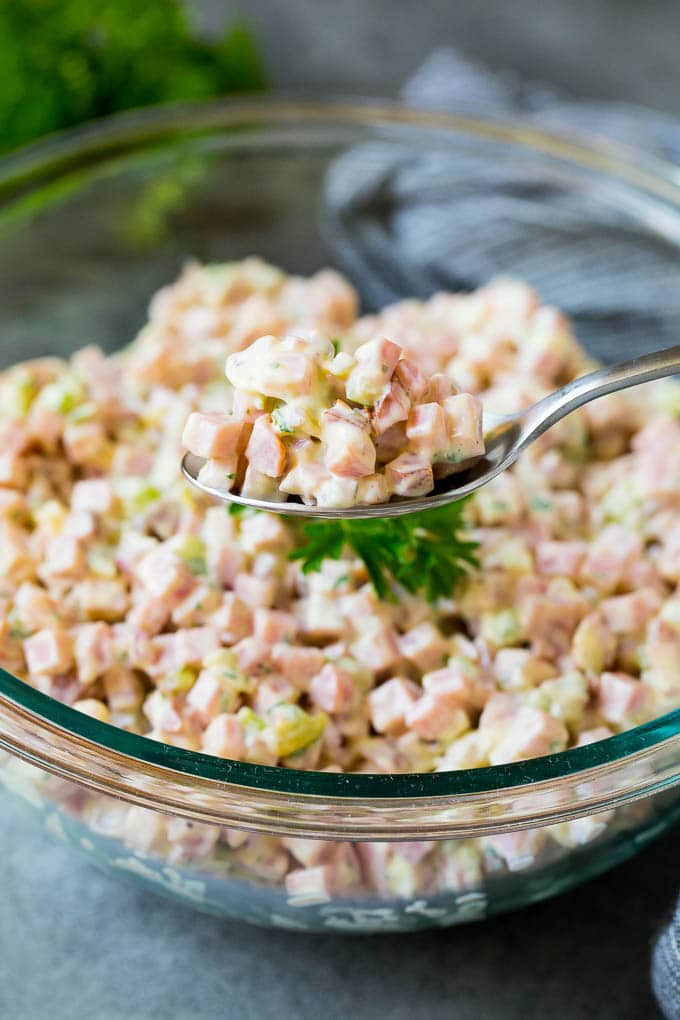 A spoon serving up a portion of diced ham and vegetables in a creamy dressing.