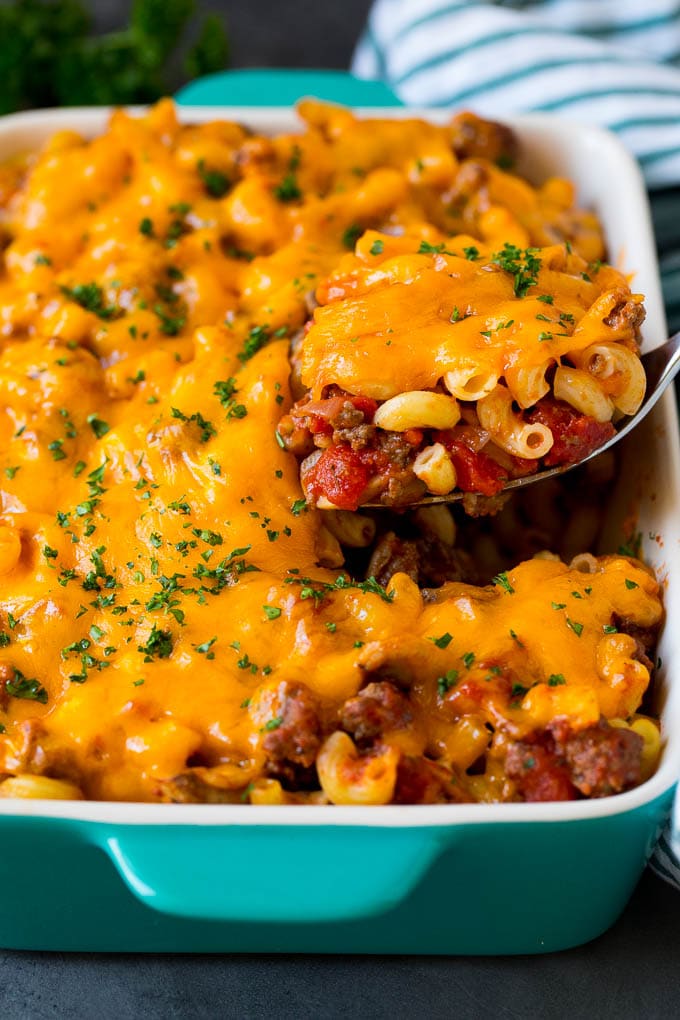 A spoon serving up a portion of hamburger casserole made with pasta and melted cheese.