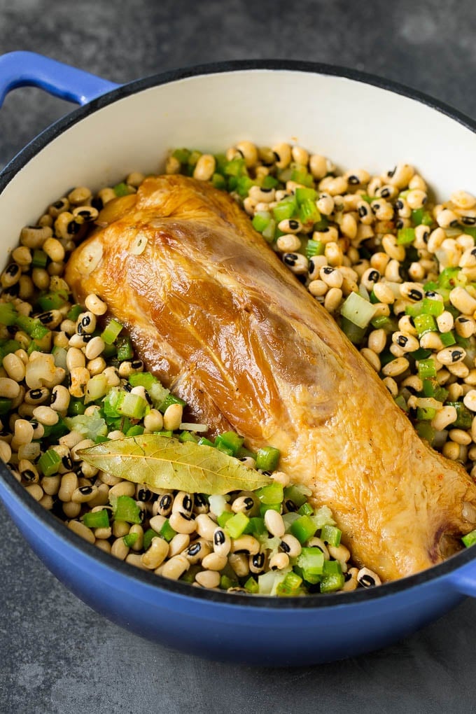 A ham shank in a pot of black eyed peas and vegetables.