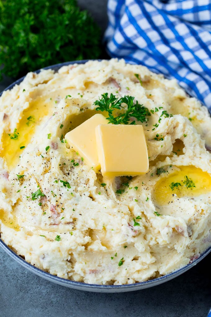 A bowl of red mashed potatoes with butter and chopped herbs.