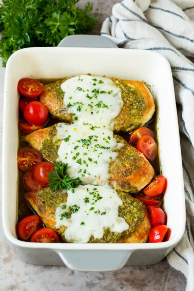 Pesto chicken in a baking dish with melted cheese and cherry tomatoes.