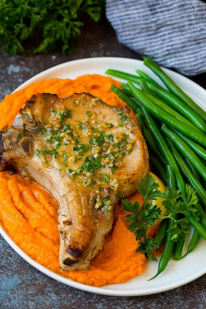 A pork chop served with sweet potatoes and green beans.