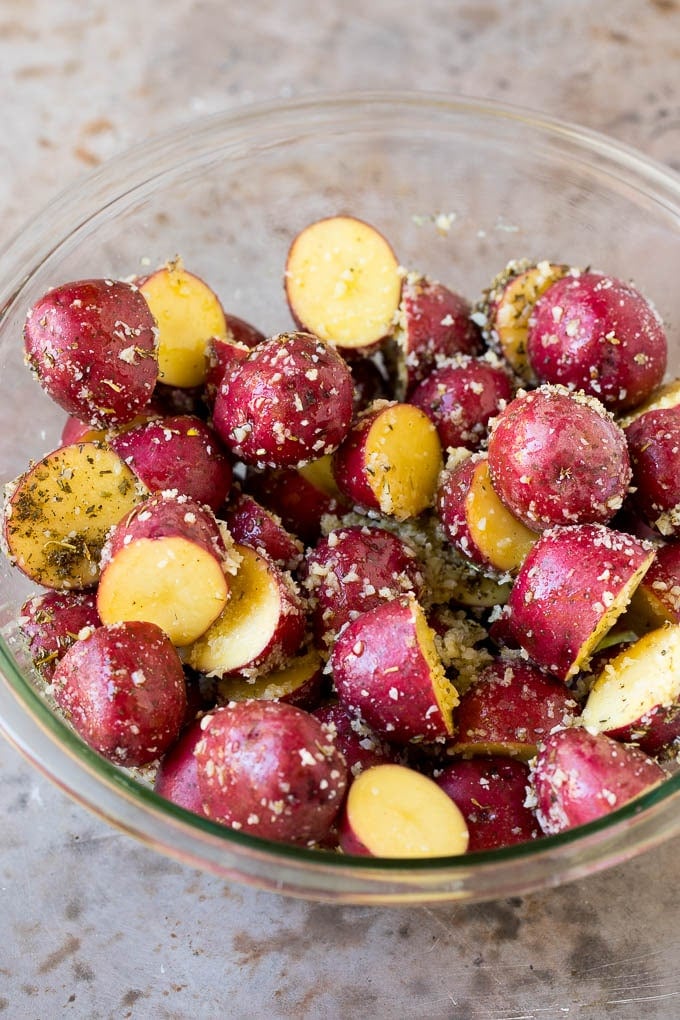 Halved potatoes in a bowl coated in olive oil and seasonings.