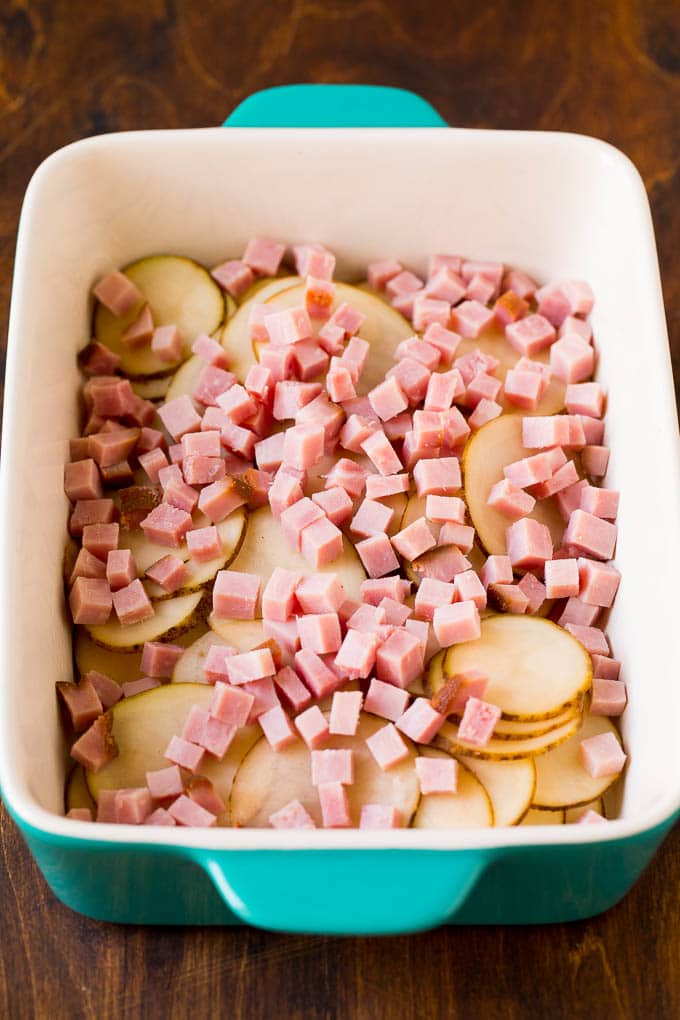 Sliced potatoes and diced ham in a baking dish.