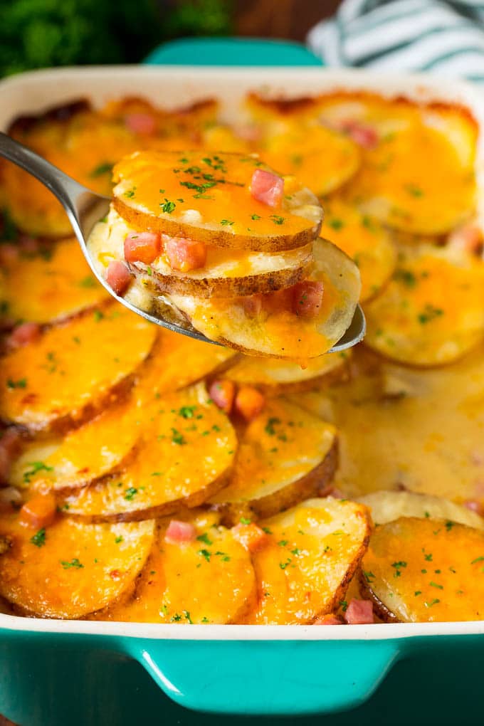 This scalloped potatoes and ham recipe is a layered casserole of thinly sliced potatoes in cheese sauce with diced ham, all baked together to golden brown perfection. A spoonful of scalloped potatoes and ham, topped with parsley.
